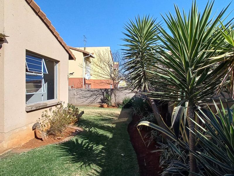 A view of the rear garden area featuring a small patio, lawn, and boundary wall, showing standard exterior finishes and maintenance requirements.