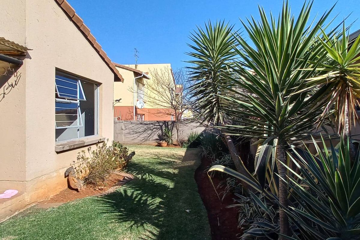 A view of the rear garden area featuring a small patio, lawn, and boundary wall, showing standard exterior finishes and maintenance requirements.