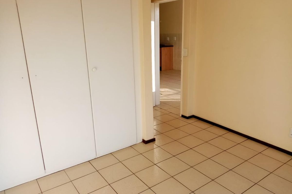 A view of an empty room featuring tiled flooring and built-in cupboards, with a doorway leading to an adjacent kitchen area.