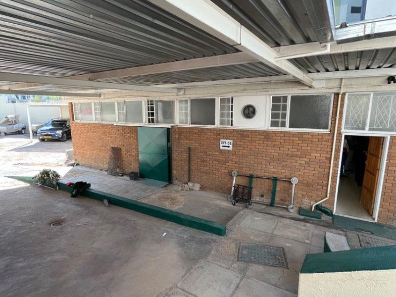 Exterior view of a commercial property featuring a covered walkway, brick facade, and paved entrance area leading to office access.