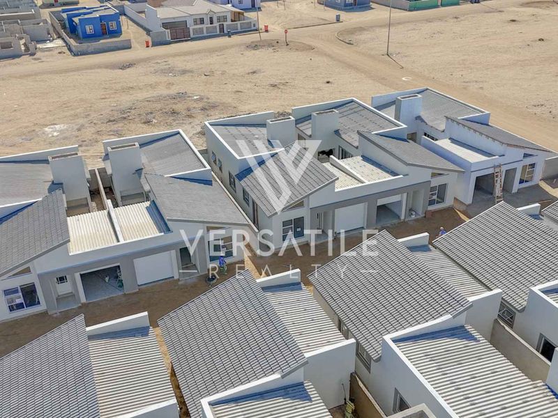 Aerial view of a modern townhouse development featuring tiled roofs, integrated garages, and perimeter boundary walls in a developing residential area.