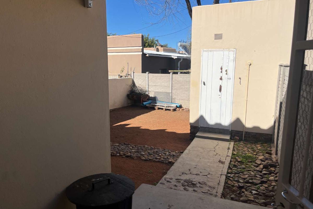 A private rear courtyard area featuring a concrete pathway, gravel landscaping, and a secure access door to the property.