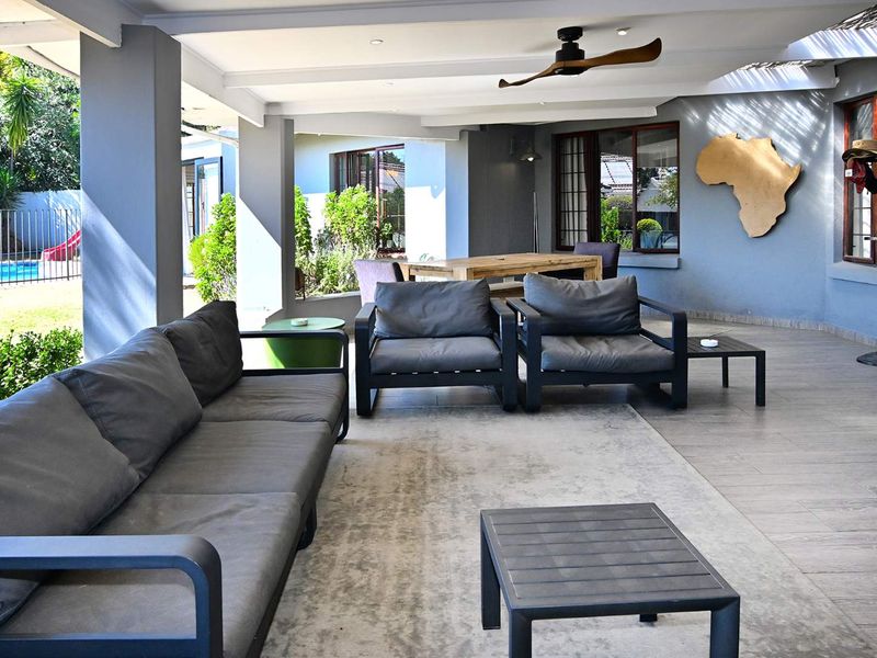Spacious covered patio featuring tiled flooring, recessed lighting, and a ceiling fan, overlooking the garden and pool area.
