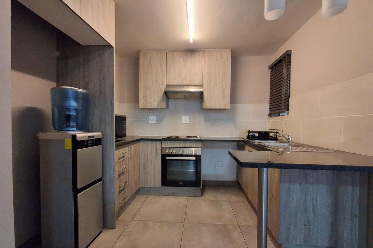 Modern kitchen featuring light wood-grain cabinetry, dark granite countertops, built-in oven, hob, extractor fan, and a breakfast bar with tiled flooring.