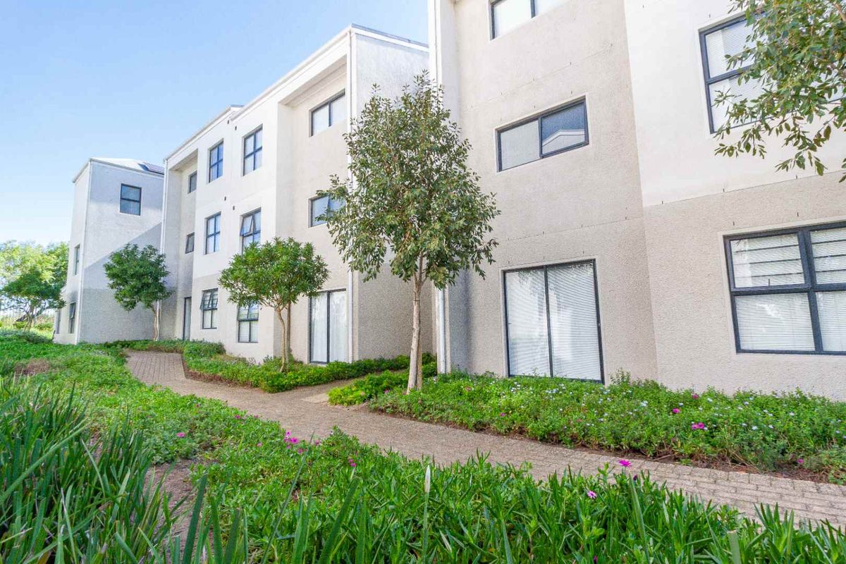 A view of the rear apartment building facade featuring a paved walkway and established garden landscaping.
