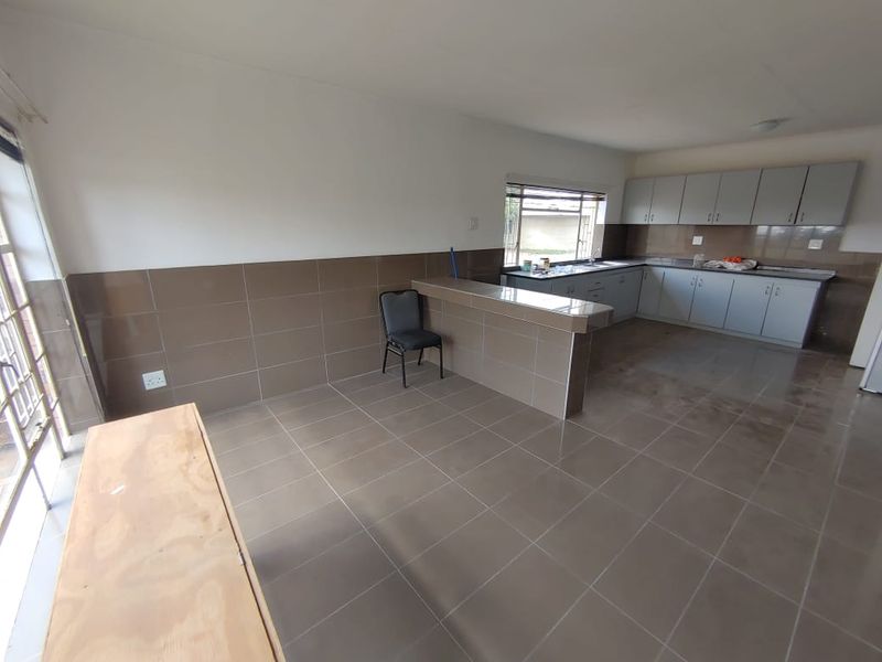 An open-plan kitchen and living area featuring tiled flooring, neutral wall tiles, and built-in cabinetry with a breakfast bar counter.