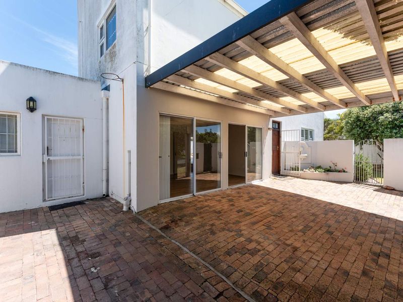 A paved outdoor patio area featuring a covered pergola structure, sliding glass door access, and a security gate.