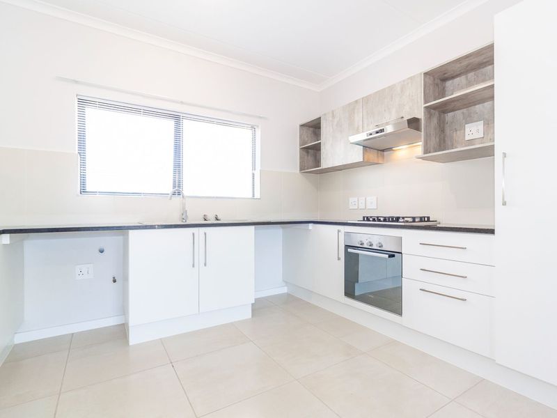 A clean, modern kitchen featuring white cabinetry, wood-look upper shelving, built-in oven, gas hob, and neutral tiled flooring.