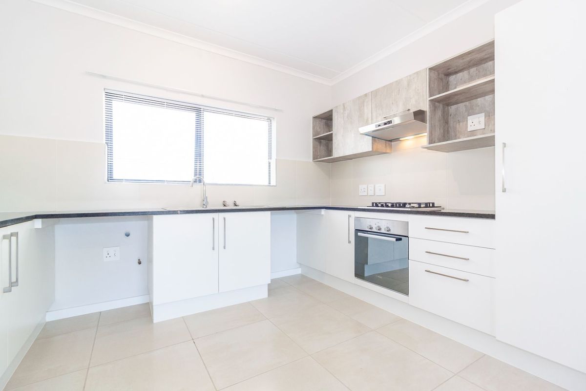 A clean, modern kitchen featuring white cabinetry, wood-look upper shelving, built-in oven, gas hob, and neutral tiled flooring.