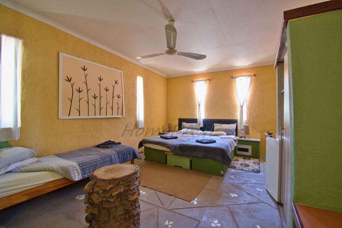 A spacious bedroom featuring textured yellow walls, a ceiling fan, and tiled flooring, providing a functional layout for guest accommodation.