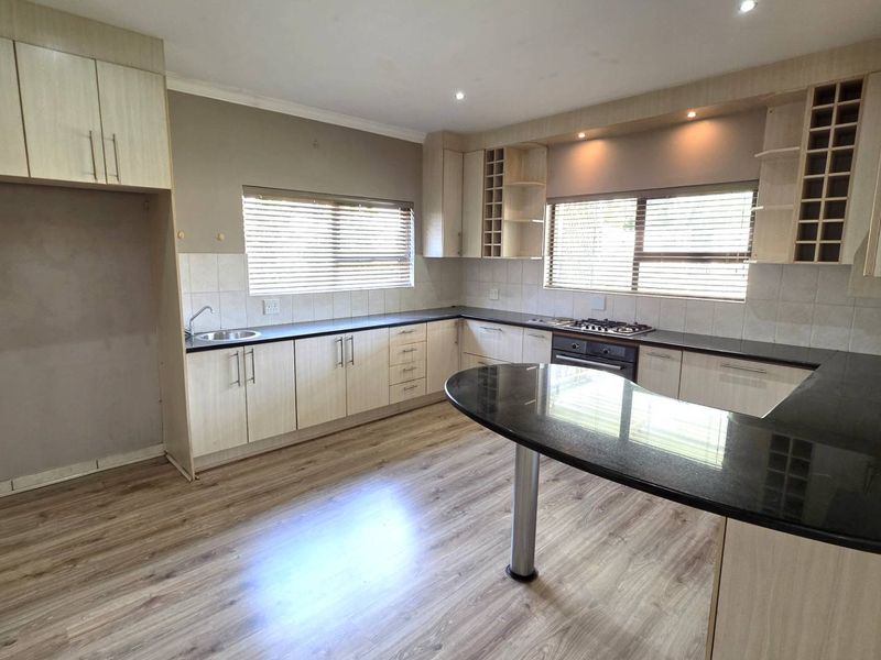 Spacious kitchen featuring light wood cabinetry, dark granite countertops, a gas hob, and integrated oven, finished with modern laminate flooring.