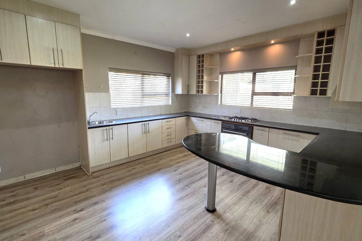 Spacious kitchen featuring light wood cabinetry, dark granite countertops, a gas hob, and integrated oven, finished with modern laminate flooring.