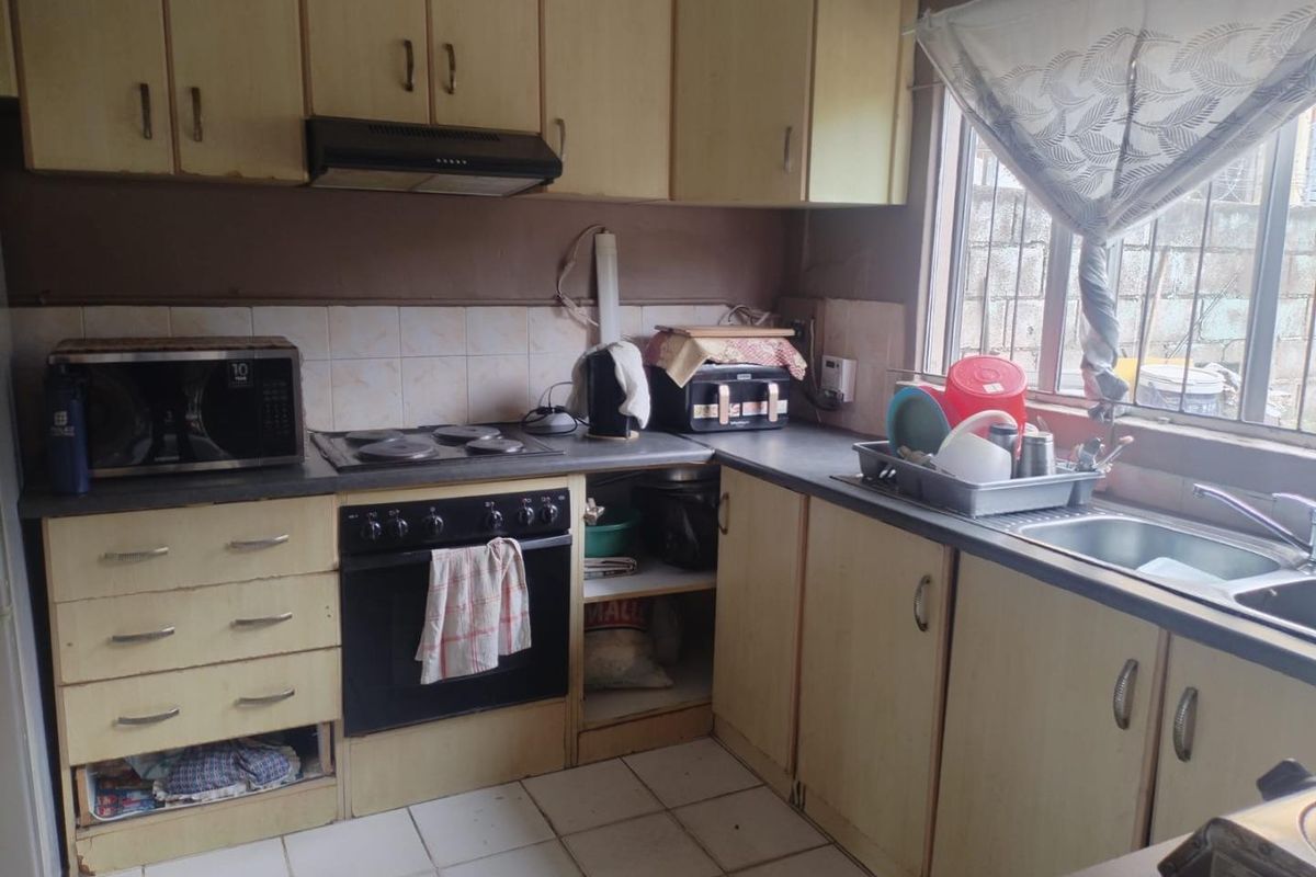 A functional kitchen featuring built-in cabinetry, an electric hob with extractor fan, and a stainless steel sink, offering potential for modernization.