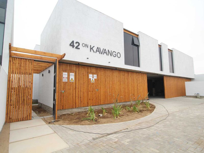 Modern townhouse exterior featuring clean white render, timber slat detailing, a timber pergola entrance, and a paved driveway at 42 on Kavango.