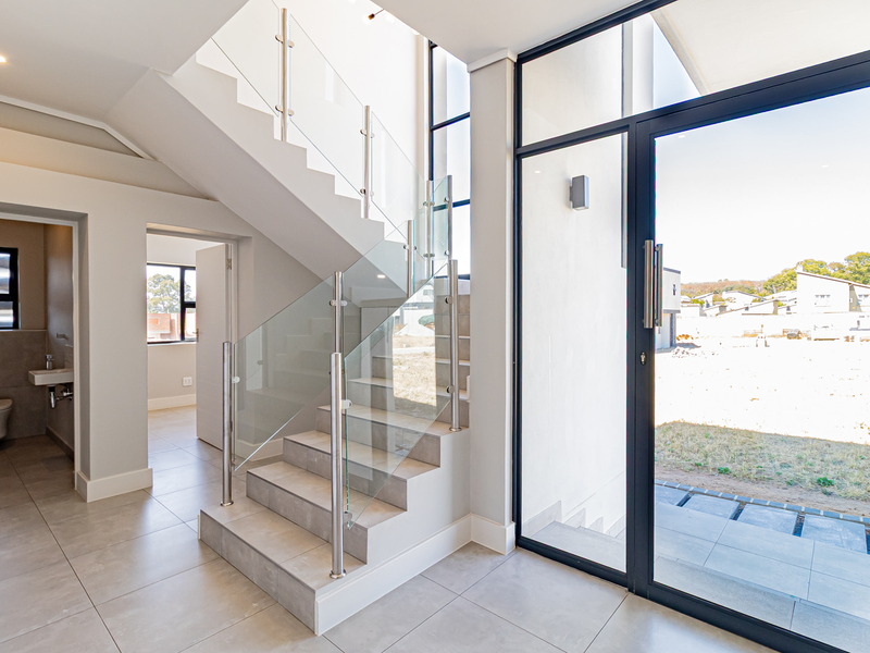 Modern entrance hall featuring a sleek tiled staircase with glass balustrade, large glass door, and access to a guest bathroom with contemporary fixtures.