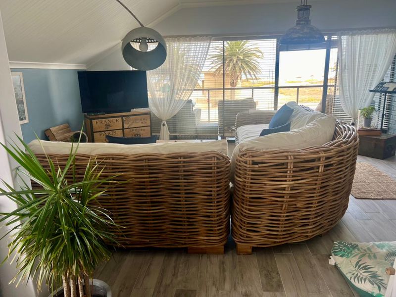A bright living room featuring vaulted ceilings, wood-look tile flooring, and large sliding glass doors that open onto a balcony with coastal views.