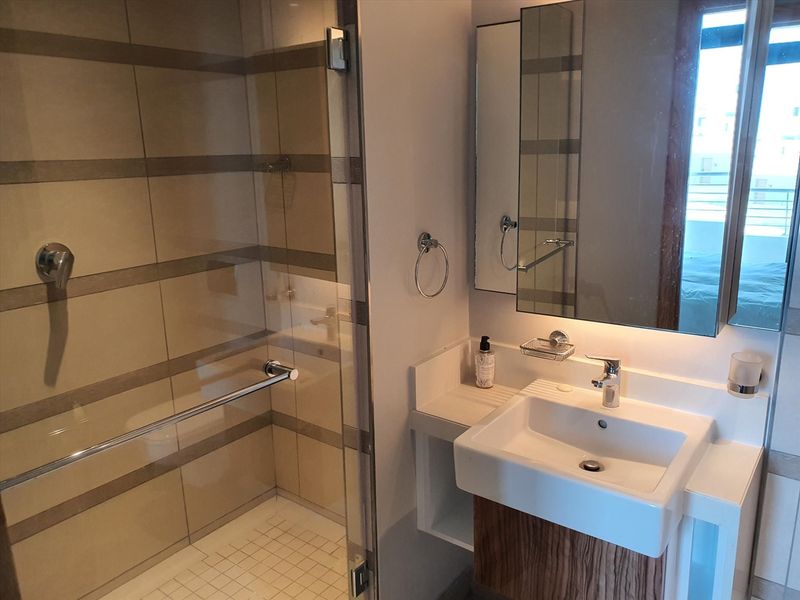 A modern bathroom featuring a glass-enclosed shower with tiled walls and a vanity basin with a wall-mounted mirror.