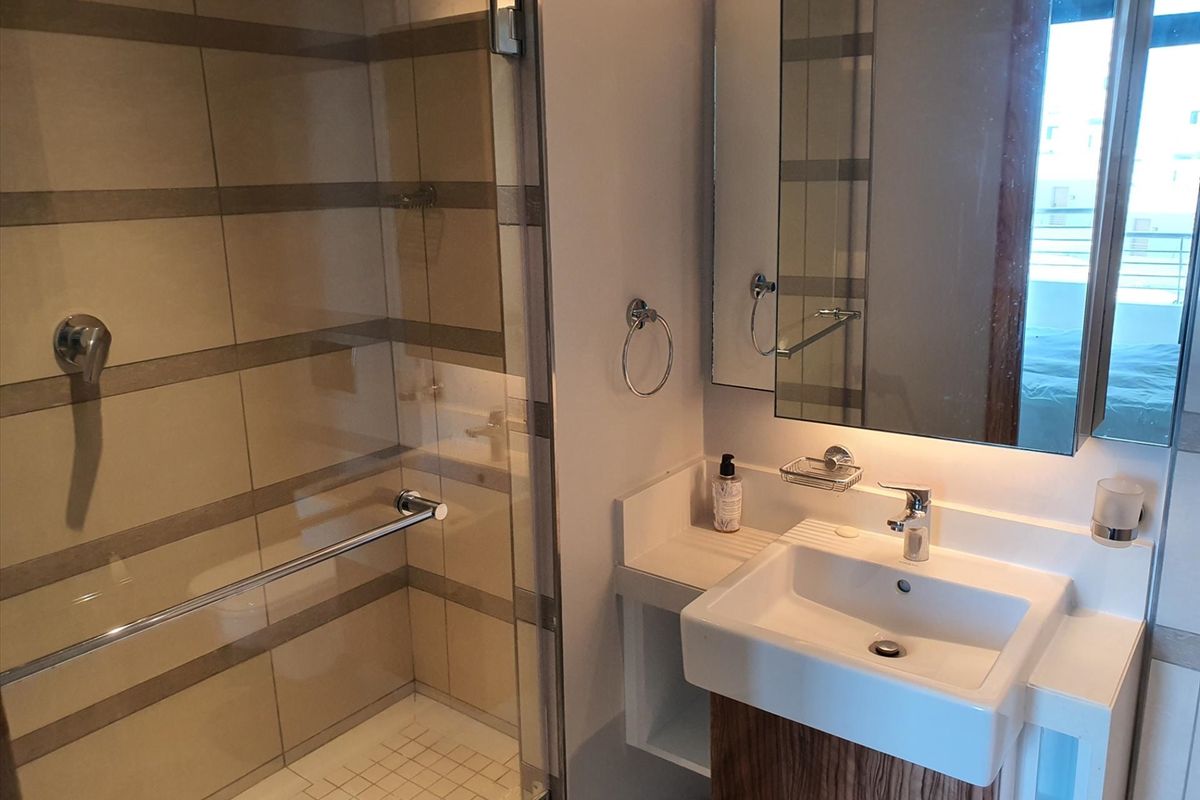 A modern bathroom featuring a glass-enclosed shower with tiled walls and a vanity basin with a wall-mounted mirror.