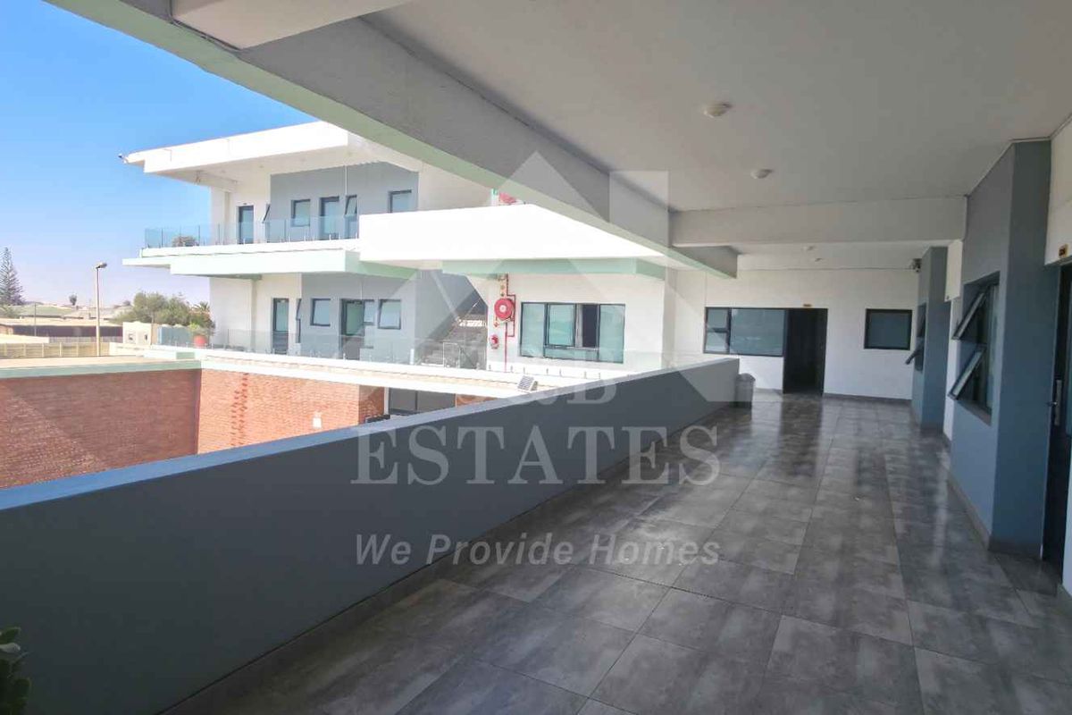 A spacious covered balcony area with tiled flooring and modern aluminium window frames, offering an open view of the surrounding property exterior.