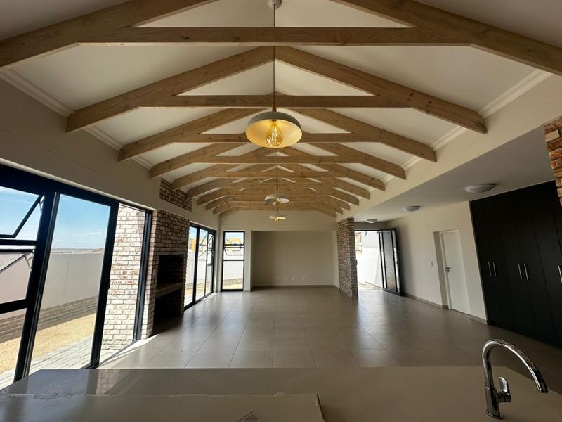 Spacious open-plan living area featuring a vaulted ceiling with exposed timber trusses, tiled floors, a built-in brick fireplace, and large sliding doors to the exterior.