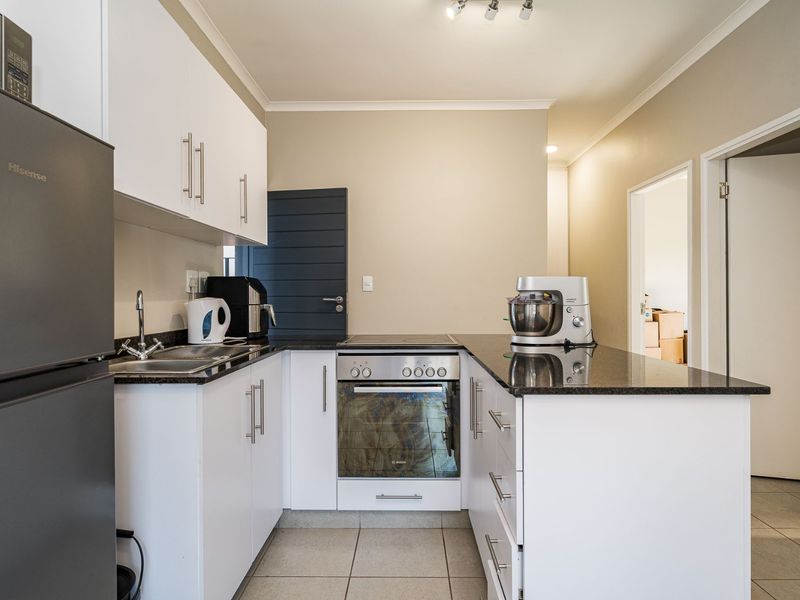 A functional kitchen featuring white cabinetry, granite countertops, a built-in oven, and an electric hob, complemented by neutral wall tones and tiled flooring.