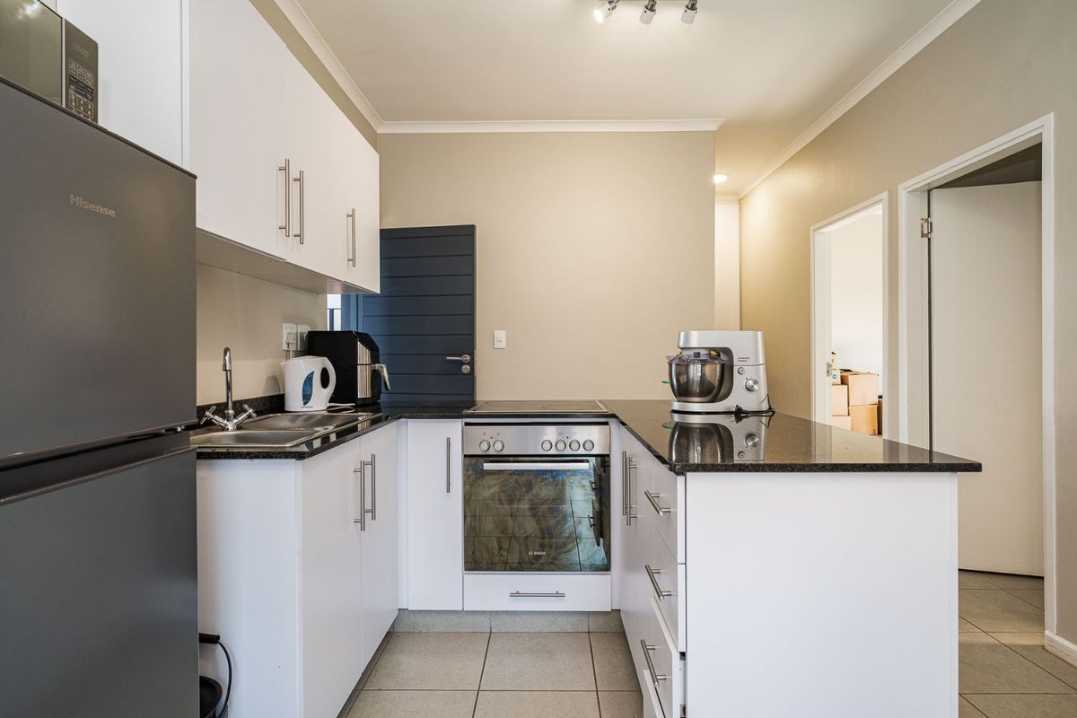 A functional kitchen featuring white cabinetry, granite countertops, a built-in oven, and an electric hob, complemented by neutral wall tones and tiled flooring.