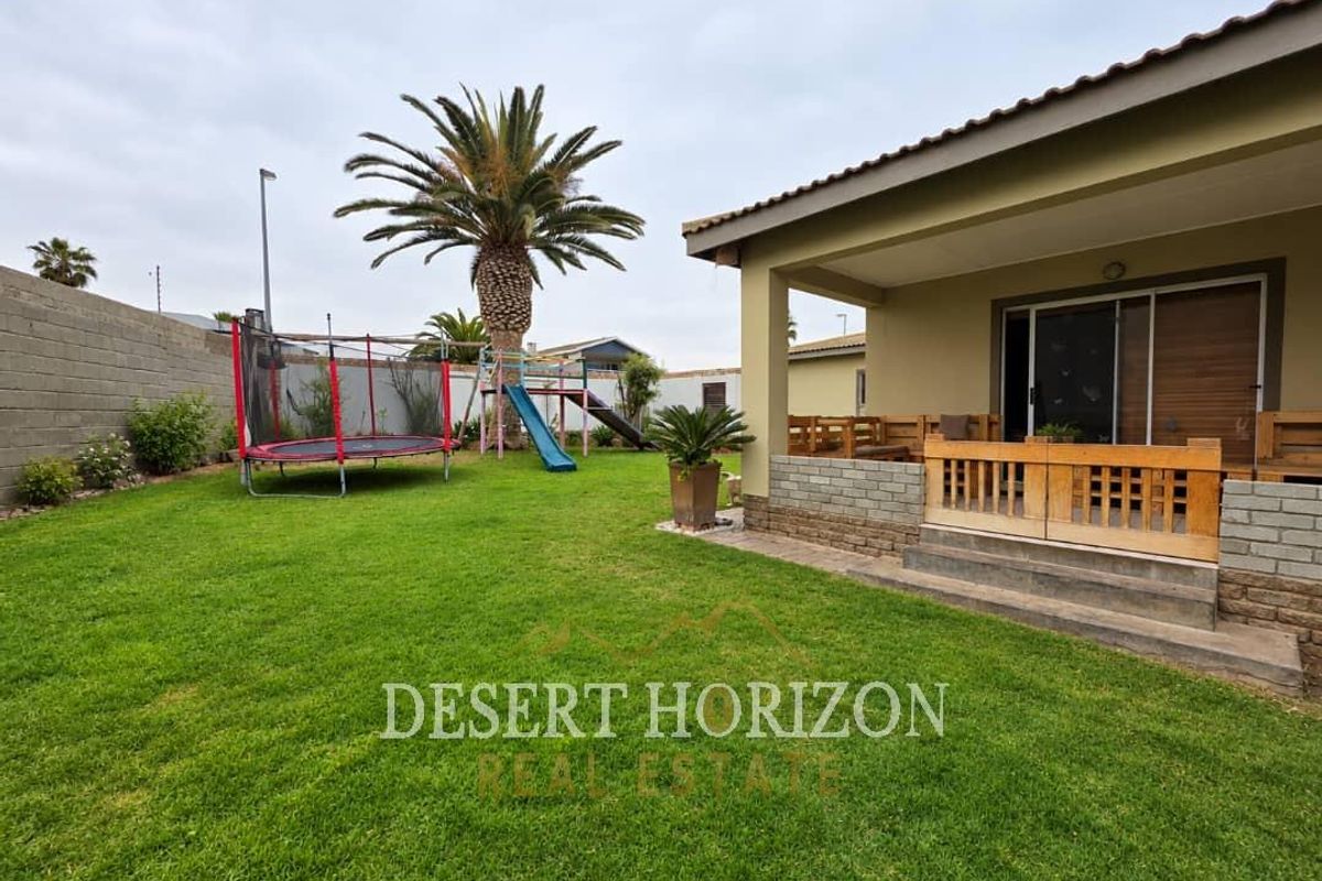 Rear view of the property featuring a covered patio, concrete steps, and a well-maintained lawn area with boundary walling.