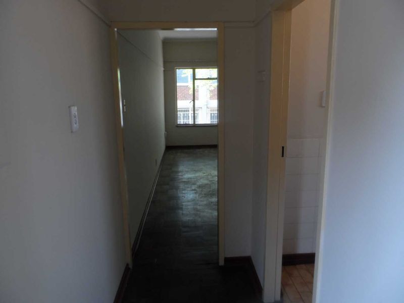A view through a hallway leading to a bedroom, featuring parquet flooring and access to an adjacent bathroom area.