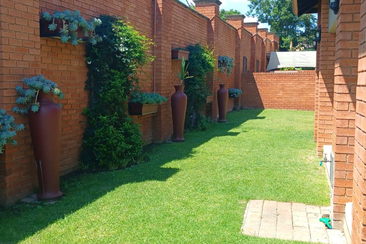 A well-maintained rear garden area featuring a brick boundary wall, manicured lawn, and a paved utility section with an outdoor water tap.