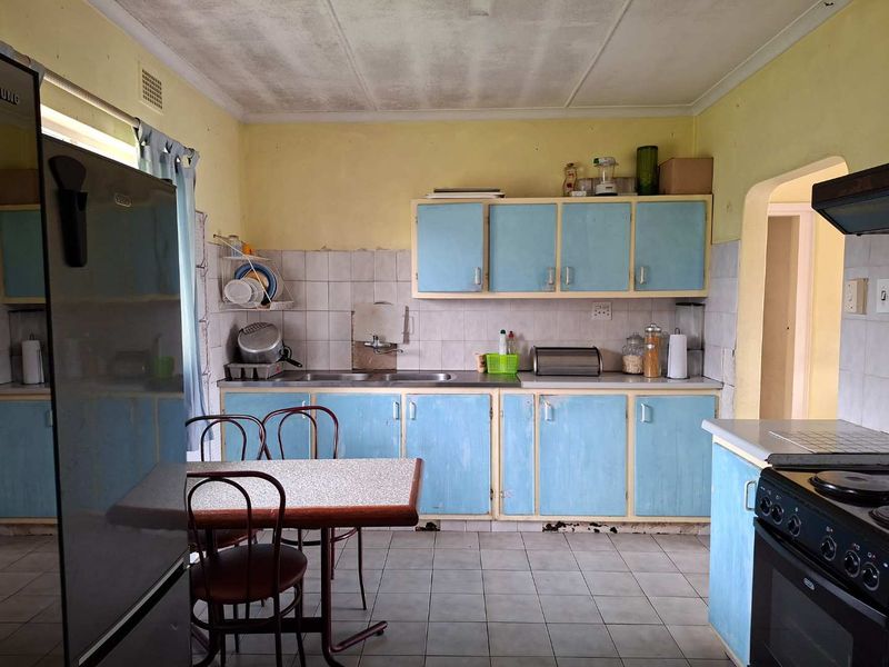 A dated kitchen featuring original blue cabinetry, tiled backsplash, and flooring, requiring cosmetic updates and repairs to the cabinetry and ceiling.