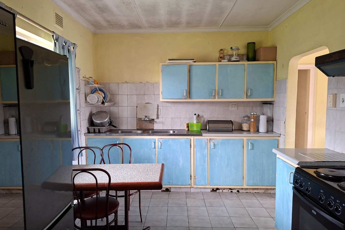 A dated kitchen featuring original blue cabinetry, tiled backsplash, and flooring, requiring cosmetic updates and repairs to the cabinetry and ceiling.