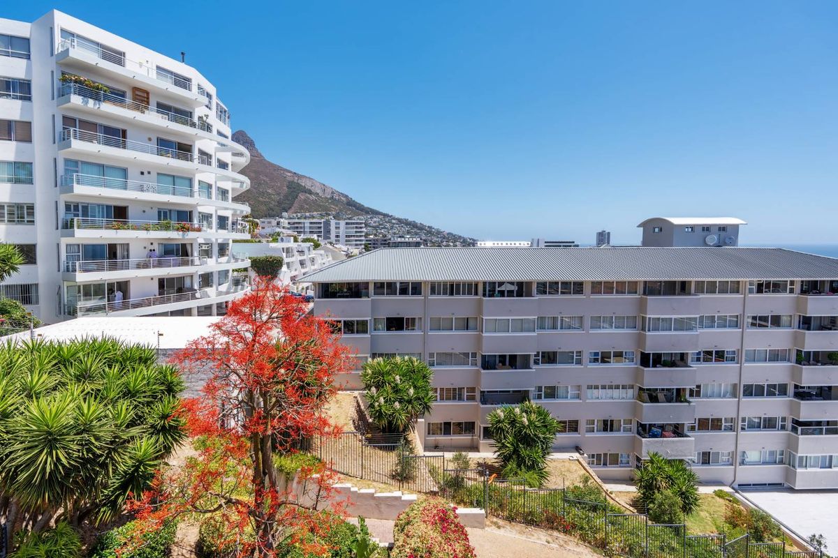 An elevated view of a multi-story apartment complex featuring private balconies, metal railings, and well-maintained surrounding garden areas.