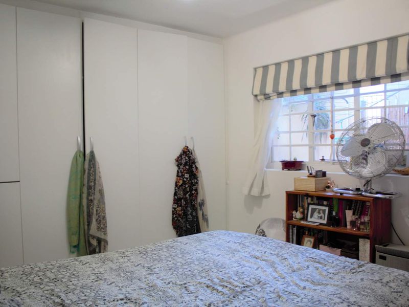 A functional bedroom featuring floor-to-ceiling built-in cupboards and a window fitted with security bars.