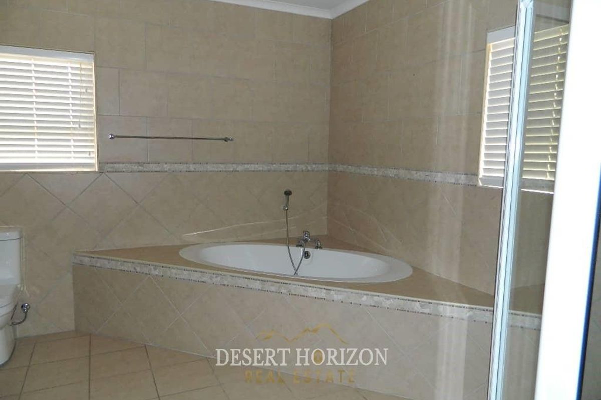 A tiled bathroom featuring a built-in corner bathtub, a toilet, and dual windows with fitted blinds.