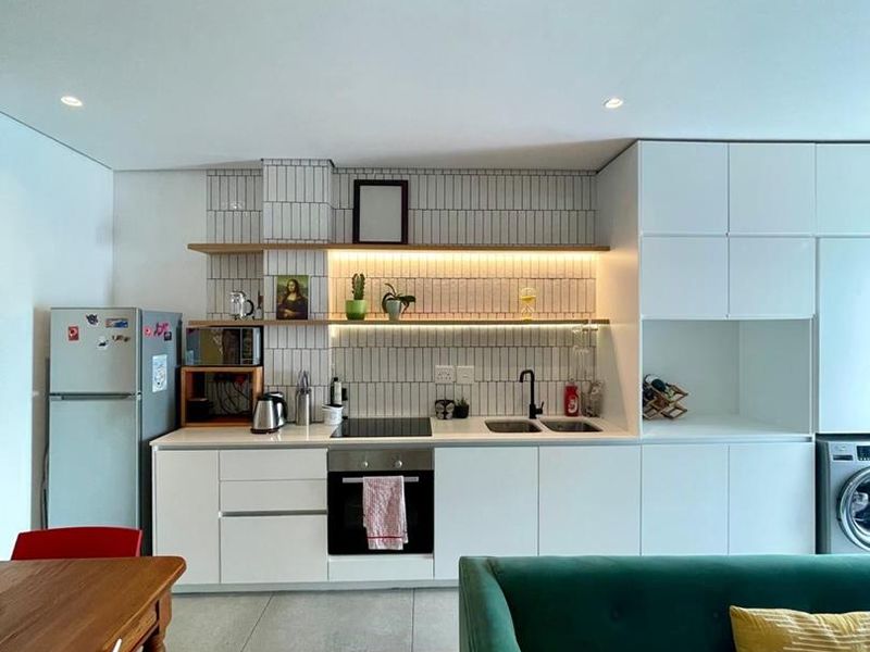 Modern open-plan kitchen featuring sleek white cabinetry, integrated appliances, tiled backsplash, and warm under-cabinet lighting, seamlessly connecting to the living and dining area.