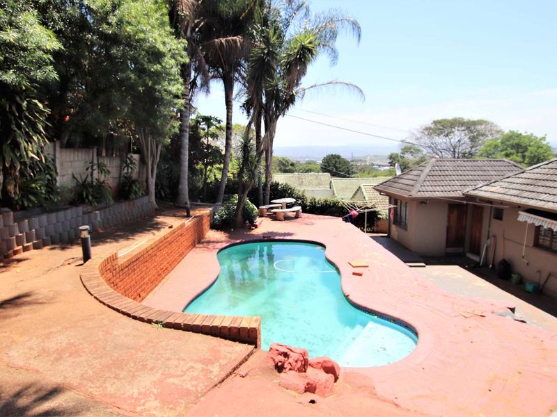 Outdoor pool area featuring a kidney-shaped swimming pool, brick retaining walls, and paved patio space, offering potential for landscaping and pool restoration.
