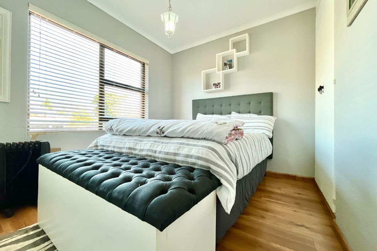 A well-maintained bedroom featuring laminate flooring, a built-in cupboard, and large windows with venetian blinds, providing ample natural light.