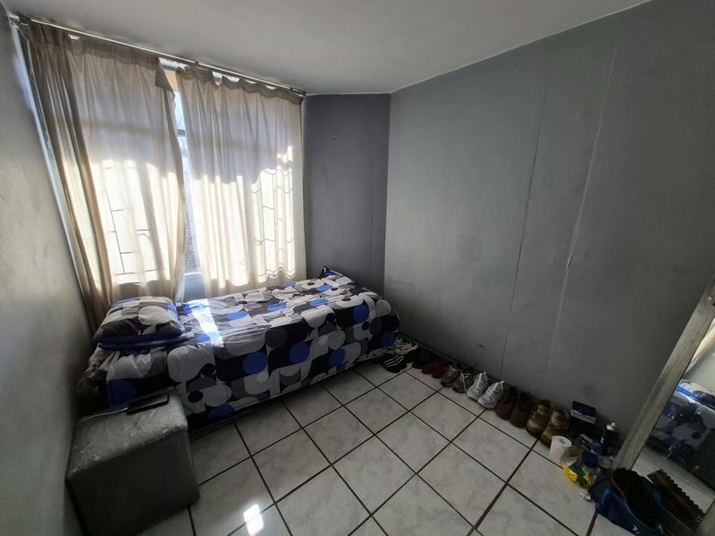 A bedroom featuring tiled flooring and large windows with curtains, requiring cosmetic updates to the wall finishes.