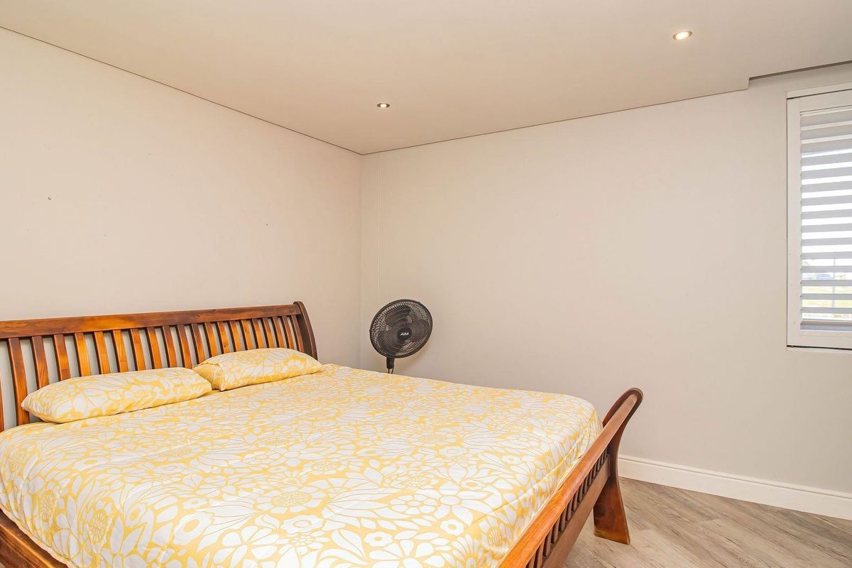 A well-maintained bedroom featuring neutral walls, wood-look flooring, recessed ceiling lighting, and white plantation shutters.
