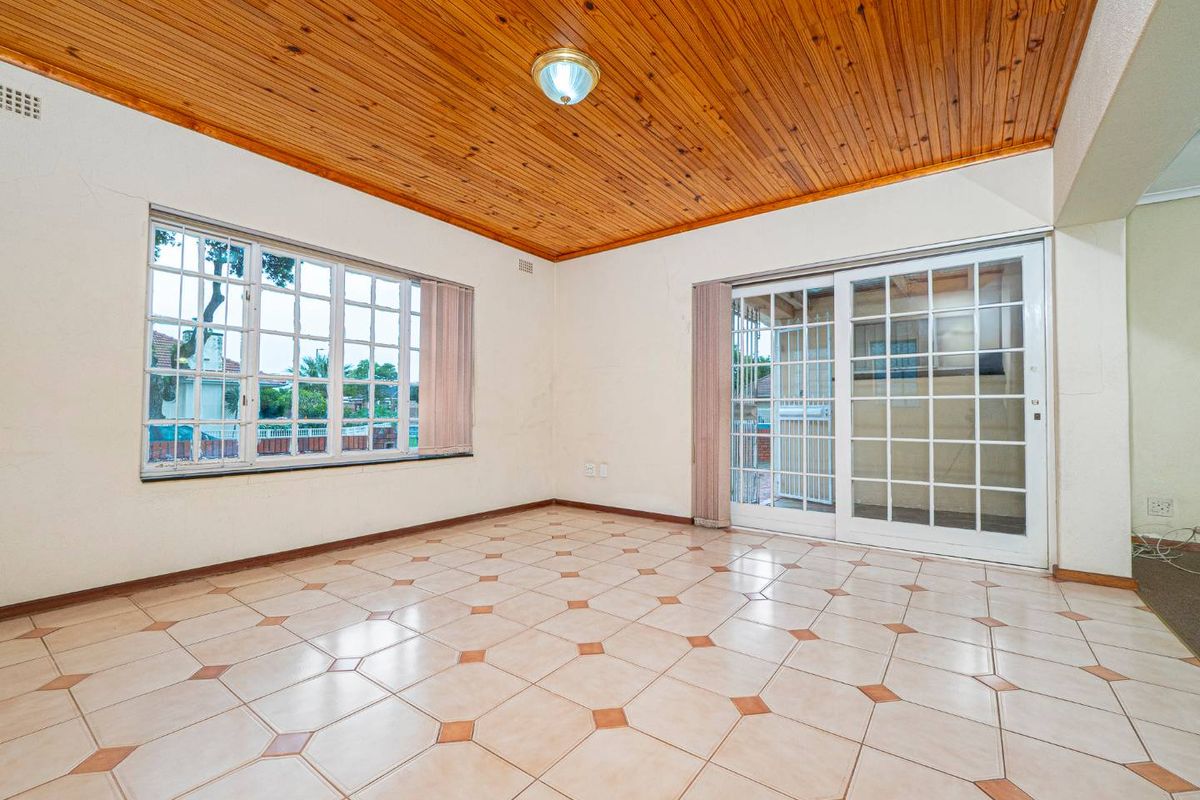 A spacious, empty living area featuring a distinctive timber-clad ceiling, tiled flooring, and large windows with sliding door access to the exterior.