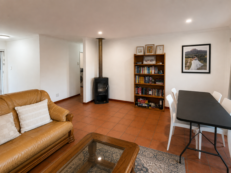 Open-plan living and dining area featuring terracotta floor tiles, a central freestanding fireplace, and recessed lighting, creating a functional and versatile living space.