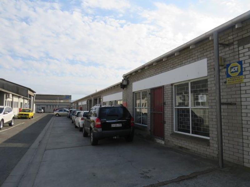 Front exterior view of an industrial unit featuring a brick facade, security gate, and concrete driveway access.