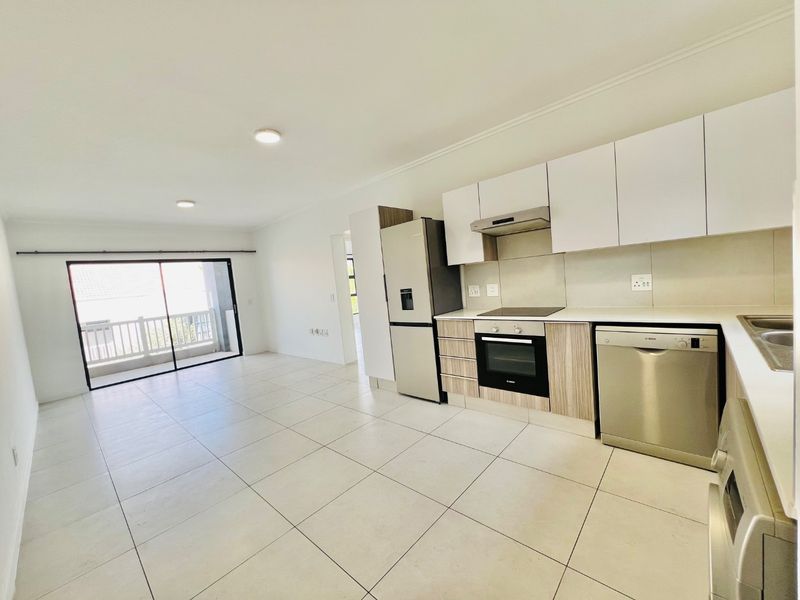 Modern open-plan kitchen and living area featuring tiled floors, sleek cabinetry, built-in appliances, and a sliding door leading to a balcony.