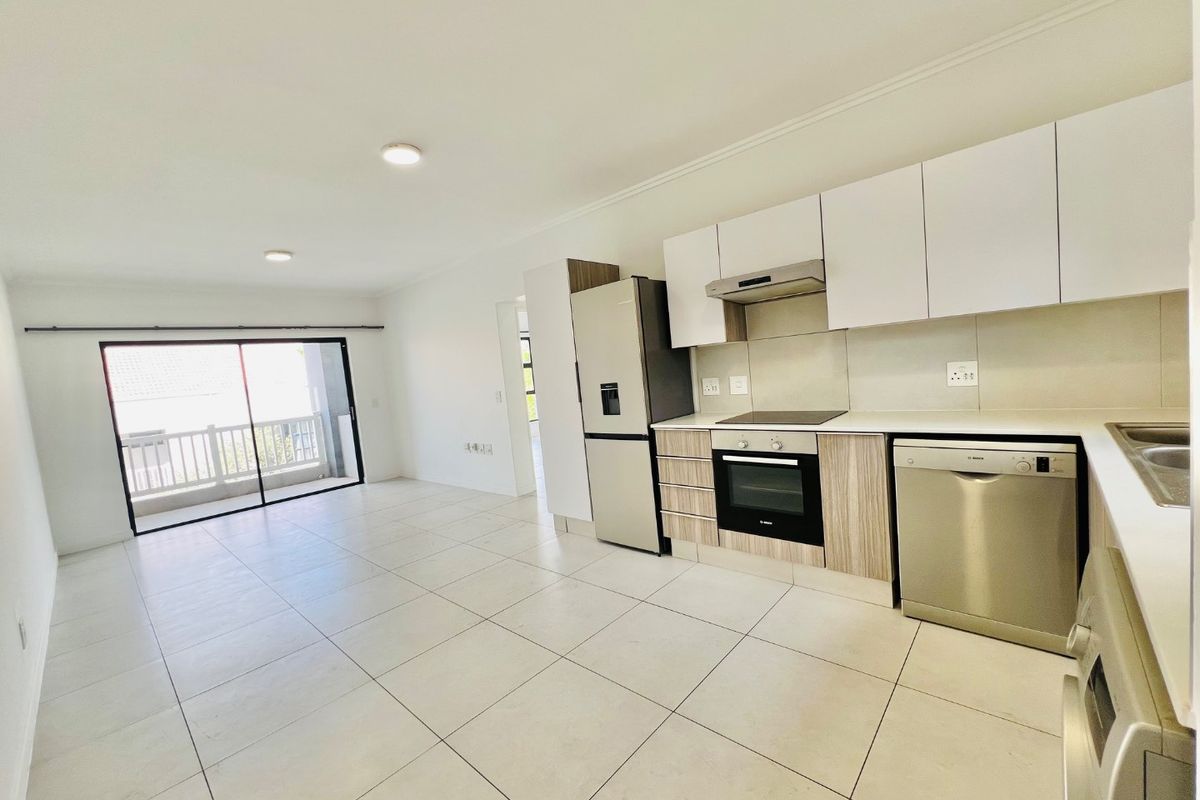 Modern open-plan kitchen and living area featuring tiled floors, sleek cabinetry, built-in appliances, and a sliding door leading to a balcony.