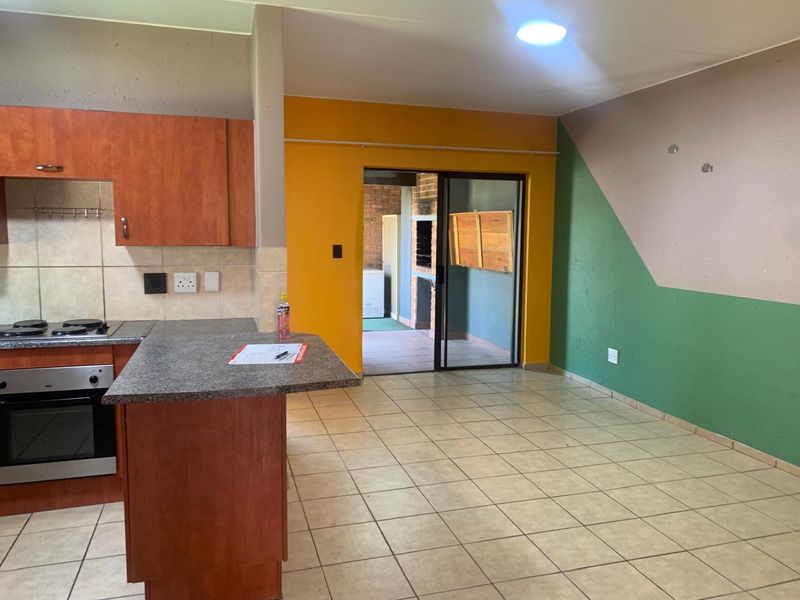 Open plan kitchen and living area featuring tiled floors, built-in oven and hob, and sliding door access to a patio with a built-in braai.