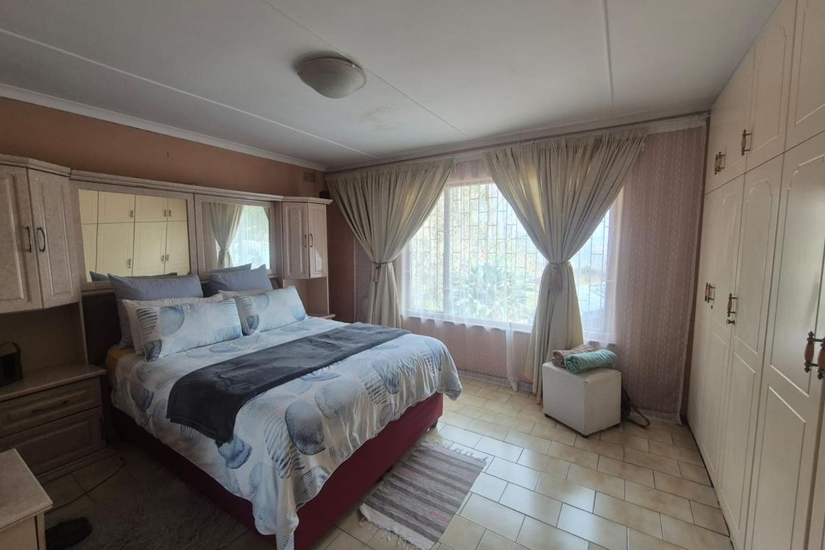 A bedroom featuring built-in cupboards, tiled flooring, and security bars on the window, offering a functional space with potential for modern updates.