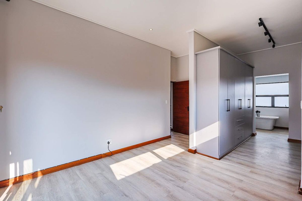 A spacious bedroom featuring light wood-look flooring, built-in cabinetry, and an open-plan layout leading to an en-suite bathroom with a freestanding bathtub.