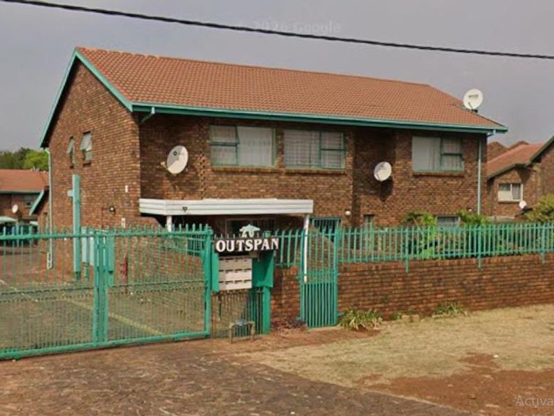 Front exterior view of a brick apartment complex featuring a secure gated entrance, tiled roofing, and communal post boxes.