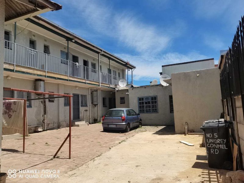Rear courtyard area featuring paved ground, metal balcony railings, and external building infrastructure including geysers and satellite dishes.