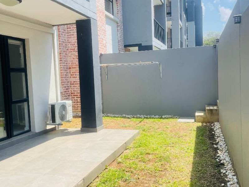 A private rear garden area featuring a tiled patio, a small lawn, and a boundary wall with a wall-mounted drying rack.